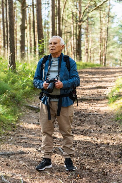 Vue de face d'un homme plus âgé voyageant avec sac à dos et appareil photo dans la nature