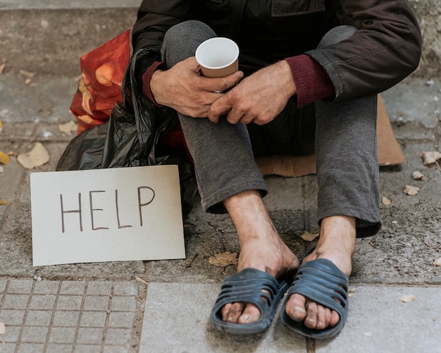 Vue de face de l'homme sans-abri à l'extérieur avec signe d'aide et tasse