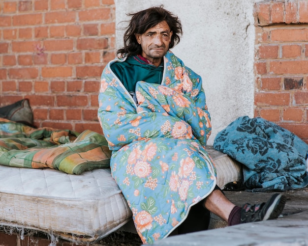 Vue de face de l'homme sans-abri sur matelas à l'extérieur sous couverture