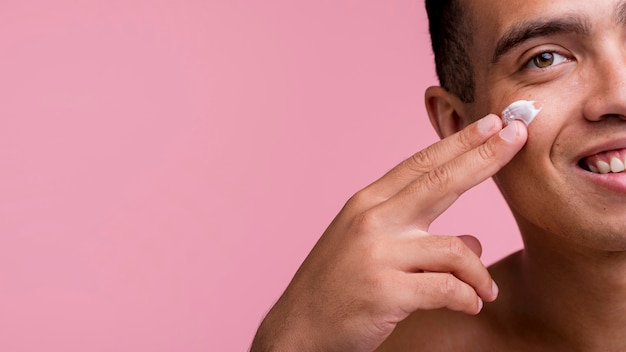 Vue de face de l'homme souriant à l'aide de crème sur le visage