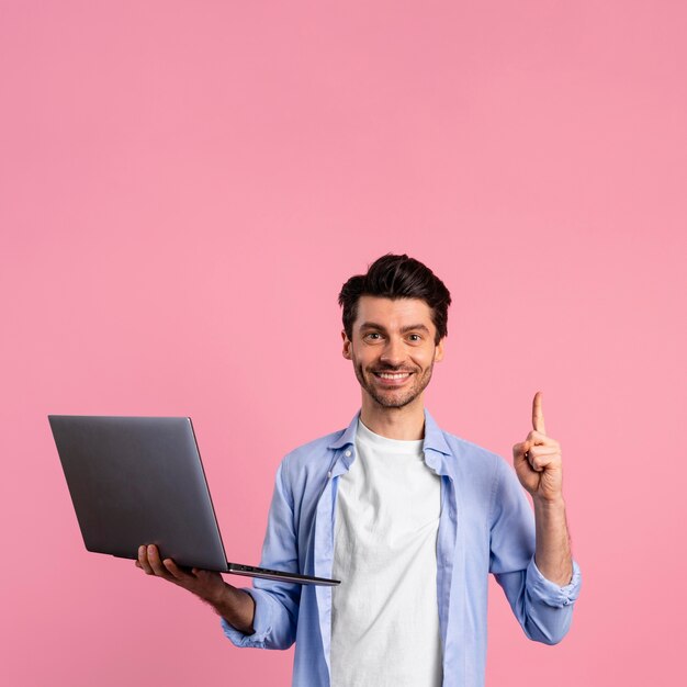 Vue de face de l'homme souriant tenant un ordinateur portable et pointant vers le haut