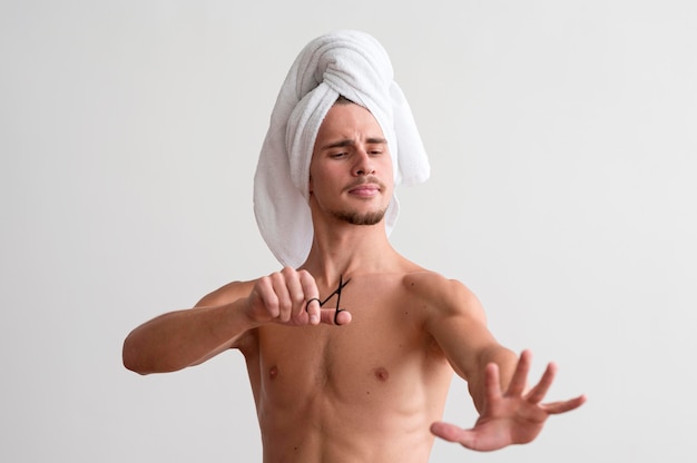 Vue de face de l'homme torse nu avec une serviette sur la tête en regardant ses ongles
