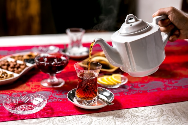 Vue de face un homme verse le thé d'une théière dans un verre d'armudu avec des tranches de citron