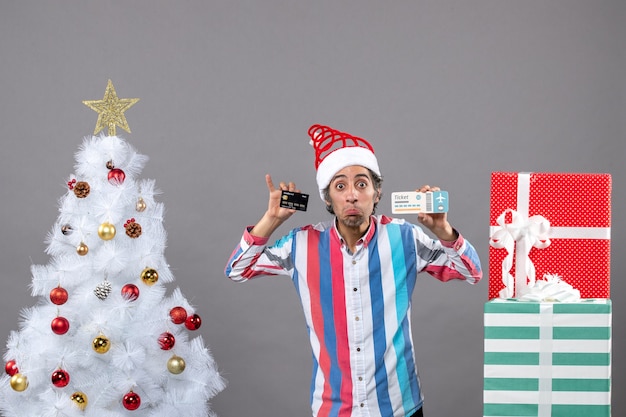 Vue de face homme avec des yeux indiscrets tenant la carte et le billet de voyage autour de l'arbre de Noël et des cadeaux