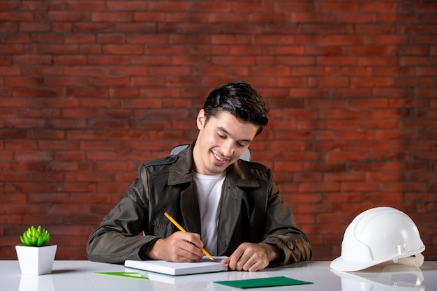 Vue de face ingénieur masculin assis derrière son lieu de travail, écrivant des notes de l'ordre du jour du constructeur d'emplois plan d'affaires document de réussite de l'entrepreneur d'entreprise