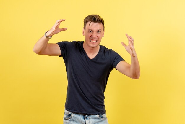 Vue de face jeune beau mâle en t-shirt foncé et jeans posant sur fond jaune modèle de couleur masculine émotions humaines