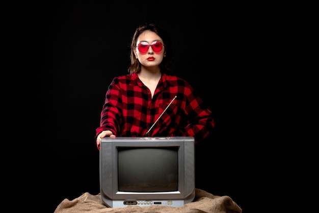 Une vue de face jeune belle dame en chemise à carreaux rouge-noir en lunettes de soleil rouges près de Little TV