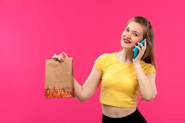 Une vue de face jeune belle dame en chemise de couleur orange pantalon noir souriant parlant au téléphone holding package