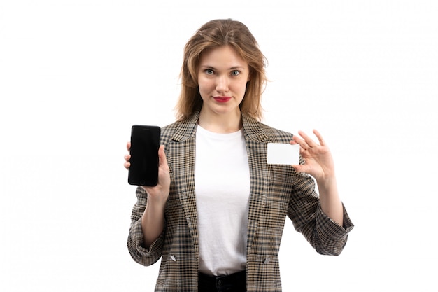 Une vue de face jeune belle dame en t-shirt blanc jeans noirs et manteau tenant un smartphone noir et une carte blanche sur le blanc