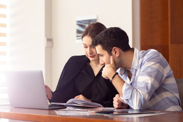 Une vue de face jeune belle femme d'affaires en chemise noire veste noire avec jeune homme à l'aide de son ordinateur portable argent discuter des problèmes à l'intérieur de son travail de bureau bâtiment de l'emploi