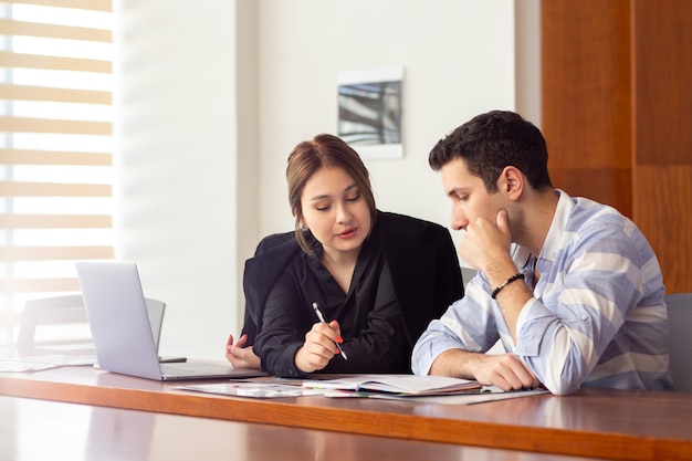 Une vue de face jeune belle femme d'affaires en chemise noire veste noire avec jeune homme discutant des problèmes de travail à l'intérieur de son bâtiment de travail de travail de bureau