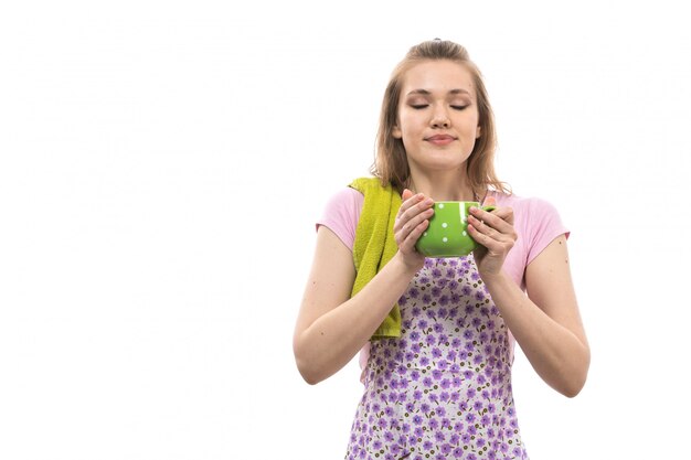 Une vue de face jeune belle femme au foyer en chemise rose cape colorée tenant une tasse verte souriant posant