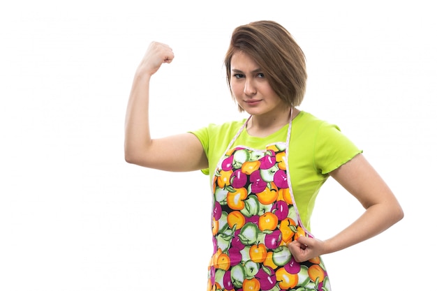 Une vue de face jeune belle femme au foyer en chemise verte cape colorée posant flexion sur le fond blanc maison cuisine féminine