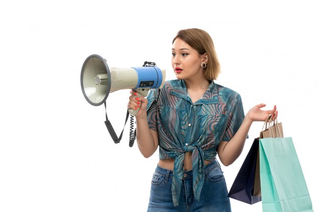 Une vue de face jeune belle femme en blouse colorée blue jeans holding shopping packages using megaphone