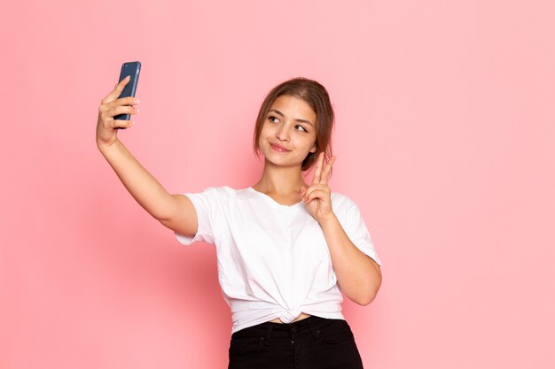Une vue de face jeune belle femme en chemise blanche posant avec une drôle d'expression et prenant un selfie