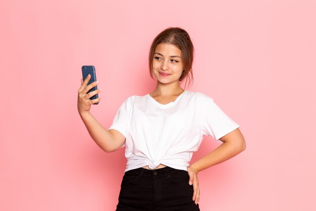 Une vue de face jeune belle femme en chemise blanche posant avec une drôle d'expression et tenant un téléphone