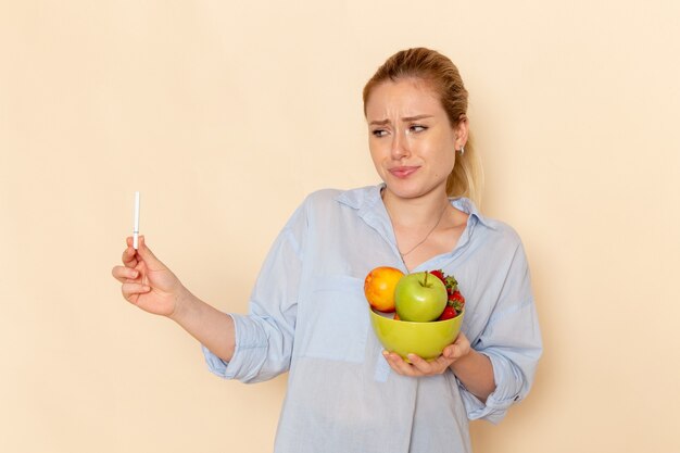 Vue de face jeune belle femme en chemise tenant la plaque avec des fruits sur le modèle de fruits mur crème légère femme pose dame