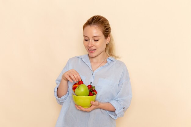 Vue de face jeune belle femme en chemise tenant la plaque avec des fruits sur le mur crème fruits mûrs modèle femme pose