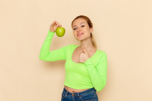 Vue de face jeune belle femme en chemise verte tenant pomme verte fraîche sur le bureau crème fruits modèle femme moelleux