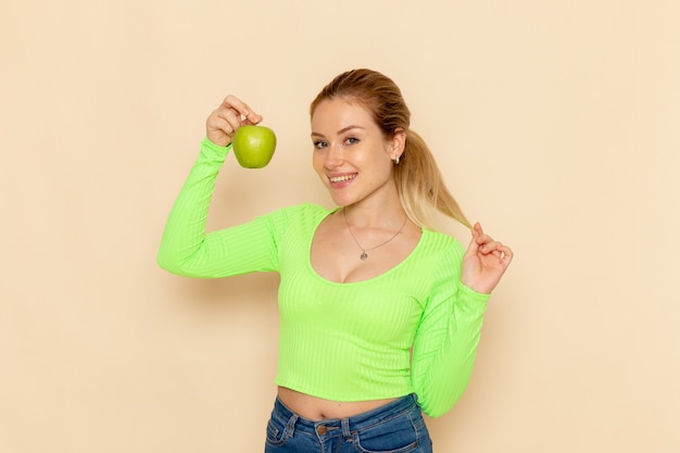 Vue de face jeune belle femme en chemise verte tenant une pomme verte fraîche sur le mur crème fruit modèle femme