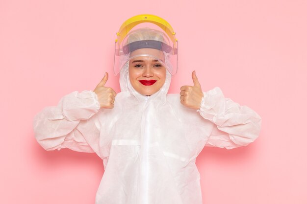 Vue de face jeune belle femme en costume blanc spécial portant un casque jaune spécial montrant comme signe sur l'espace rose costume spécial fille femme