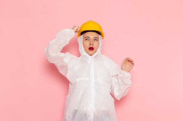 Vue de face jeune belle femme en costume blanc spécial portant un casque de protection posant et en pensant à la chimie de la femme combinaison spatiale rose