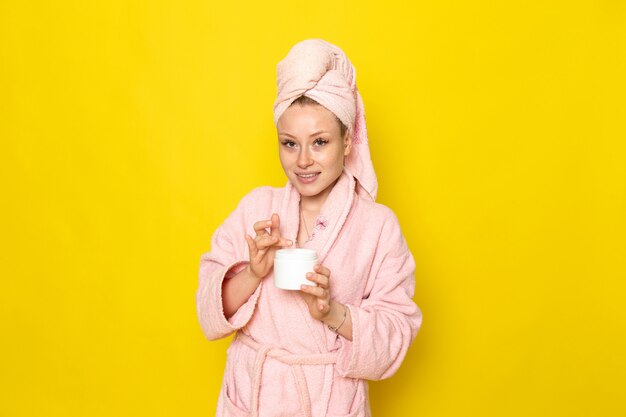 Une vue de face jeune belle femme en peignoir rose à l'aide de crème pour le visage