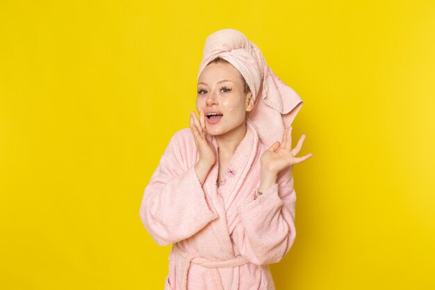 Une vue de face jeune belle femme en peignoir rose à l'aide de crème pour le visage