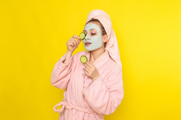 Une vue de face jeune belle femme en peignoir rose mettant des anneaux de concombre