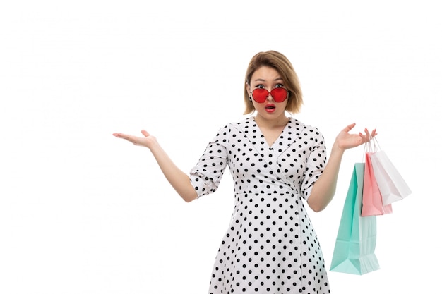 Photo gratuite une vue de face jeune belle femme en robe à pois noir et blanc en lunettes de soleil rouges tenant des colis faisant une expression surprise