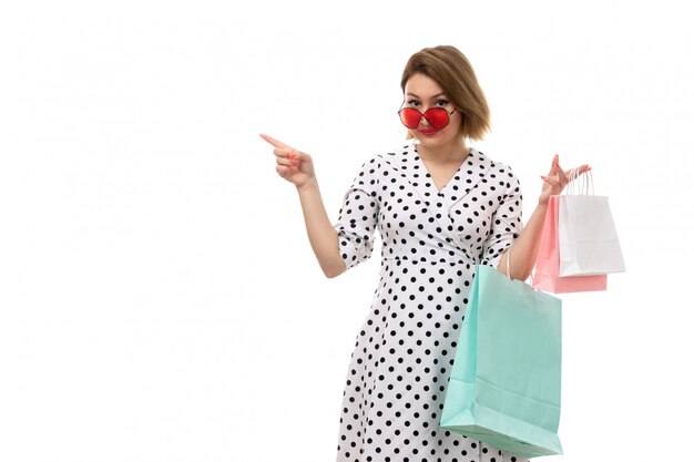 Une vue de face jeune belle femme en robe à pois noir et blanc en lunettes de soleil rouges tenant des colis posant souriant