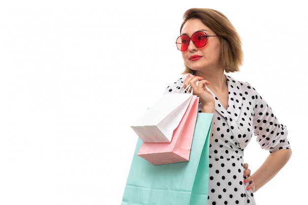 Photo gratuite une vue de face jeune belle femme en robe à pois en noir et blanc en lunettes de soleil rouges tenant des colis posant