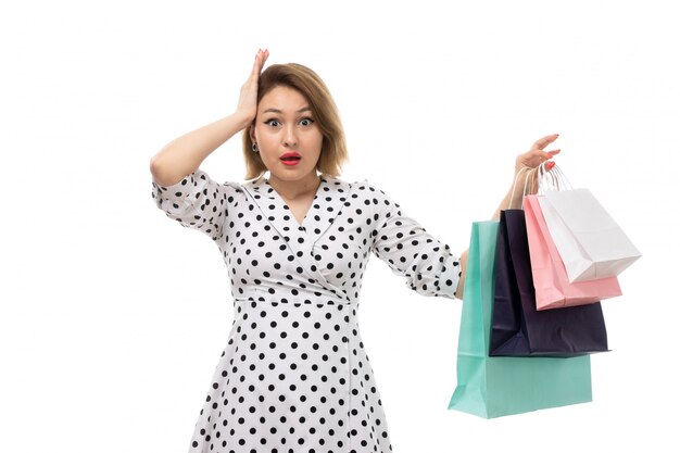 Une vue de face jeune belle femme en robe à pois noir et blanc tenant des colis shopping surpris