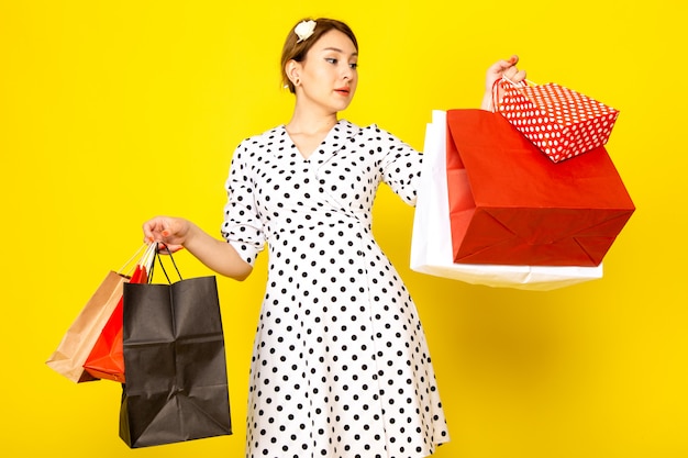 Une vue de face jeune belle femme en robe à pois noir et blanc tenant des paquets commerciaux sur jaune