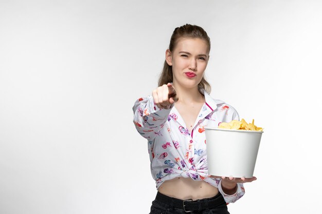 Vue de face jeune belle femme tenant des cips de pomme de terre regarder un film sur une surface blanche