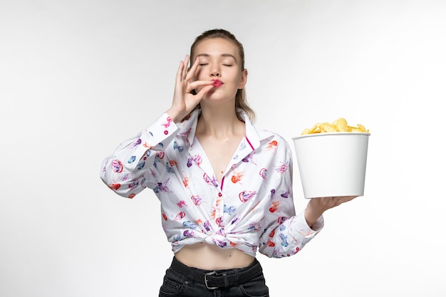 Vue de face jeune belle femme tenant des cips de pommes de terre et regarder un film sur un bureau blanc