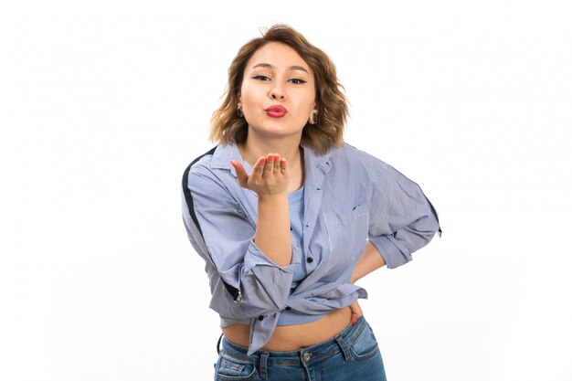 Une vue de face jeune belle fille en chemise bleue et jean bleu envoi de baisers aériens sur le blanc