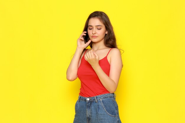 Une vue de face jeune belle fille en chemise rouge et blue-jeans parler au téléphone