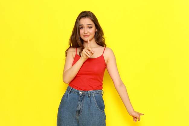 Une vue de face jeune belle fille en chemise rouge et jean bleu posant avec une expression ennuyée