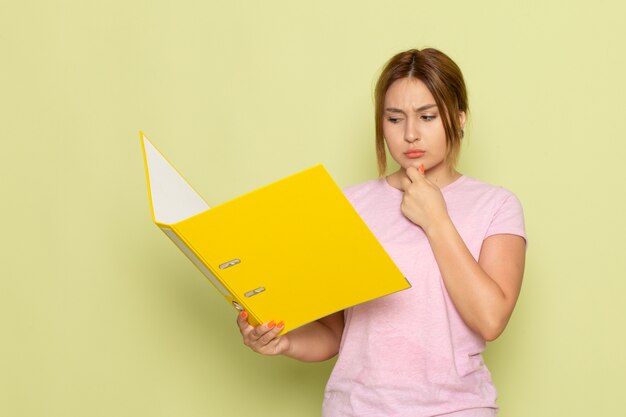 Une vue de face jeune belle fille en t-shirt rose jeans bleu lecture fichier jaune avec expression de la pensée sur le vert