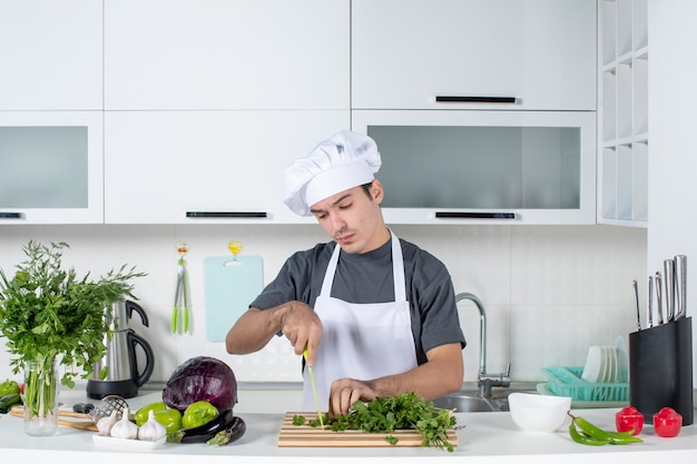 Vue de face jeune chef en uniforme coupant les verts sur la table