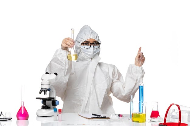 Vue de face jeune chimiste en combinaison de protection spéciale tenant le flacon avec une solution sur fond blanc clair virus de chimie covid