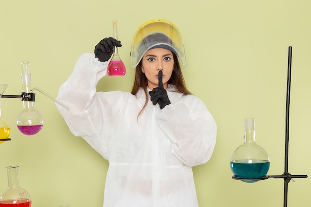 Vue de face jeune chimiste en combinaison de protection spéciale travaillant avec des solutions sur le mur vert chimie chimie emploi femelle laboratoire scientifique