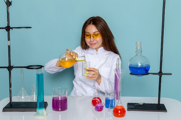 Vue de face de la jeune chimiste en costume blanc devant la table travaillant avec des solutions et souriant