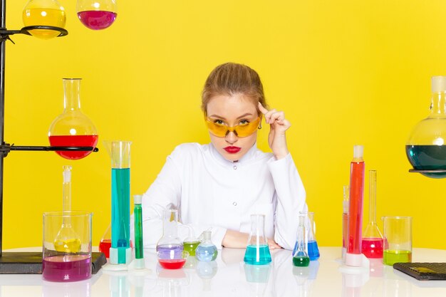 Vue de face jeune chimiste en costume blanc en face de la table avec des solutions ed travaillant avec eux se mélangeant sur le travail de science chimie de l'espace jaune