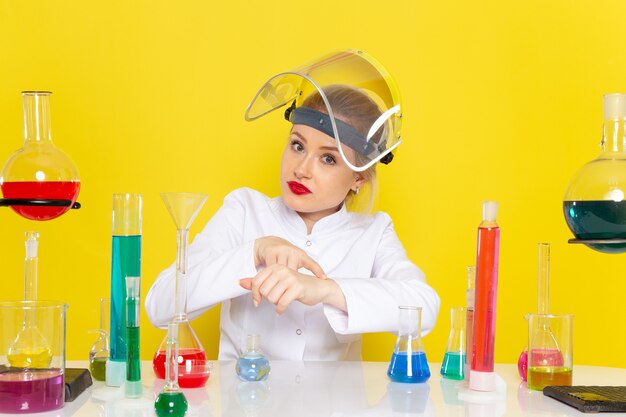 Vue de face jeune chimiste en costume blanc avec des solutions ed décoller casque montrant l'heure sur la science de la chimie de l'espace jaune s