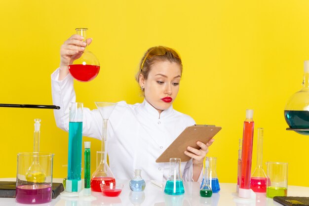 Vue de face jeune chimiste en costume blanc avec des solutions ed travaillant avec eux et assis sur le travail de processus de science chimie de l'espace jaune