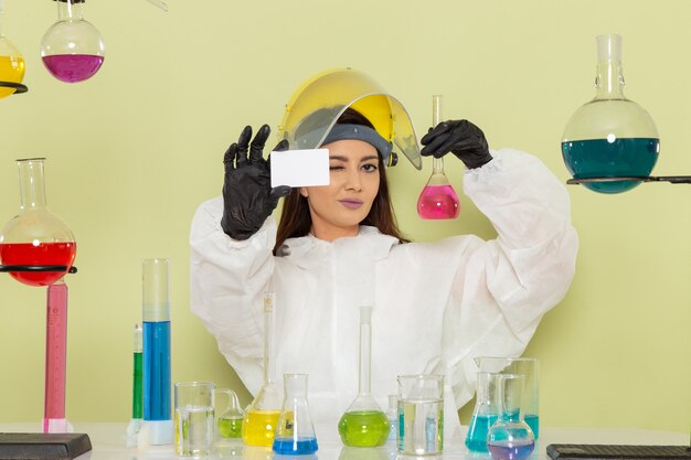 Vue de face jeune chimiste en tenue de protection spéciale tenant la carte et la solution sur le mur vert chimie laboratoire chimie emploi femelle science