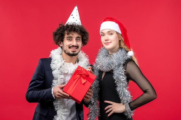 Vue de face jeune couple avec présent célébrant sur le mur rouge fête d'amour de Noël