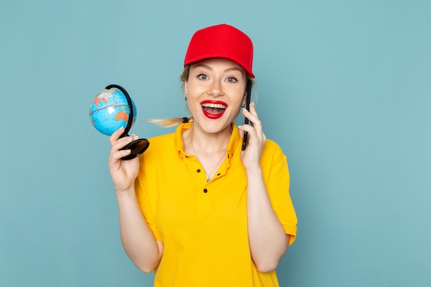 Vue de face jeune courrier en chemise jaune et cape rouge parlant au téléphone en souriant sur l'espace bleu